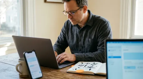 A person composes a targeted cold email on a laptop beside a notebook shortlist of a few names and a phone showing a prospect